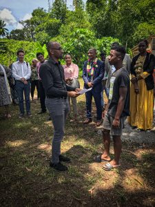 un homme remet un diplôme à un jeune homme en présence de nombreuses personnes en arrière plan